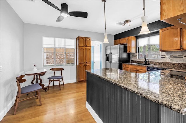kitchen with brown cabinets, a sink, stainless steel refrigerator with ice dispenser, light wood-style flooring, and baseboards