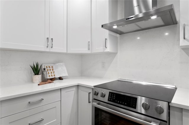 kitchen with stainless steel electric range oven, wall chimney exhaust hood, light countertops, and white cabinetry
