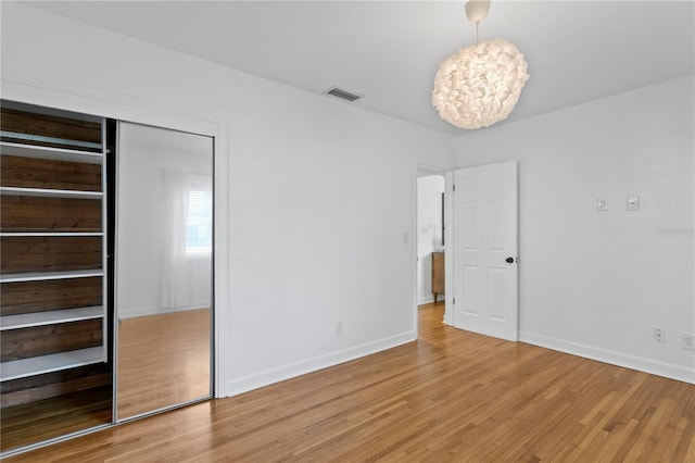 unfurnished bedroom with baseboards, visible vents, a notable chandelier, light wood-style floors, and a closet