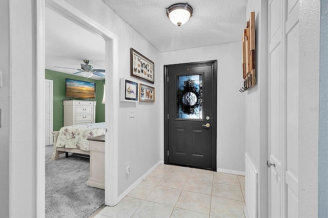 foyer entrance featuring a textured ceiling, baseboards, a ceiling fan, and light tile patterned floors