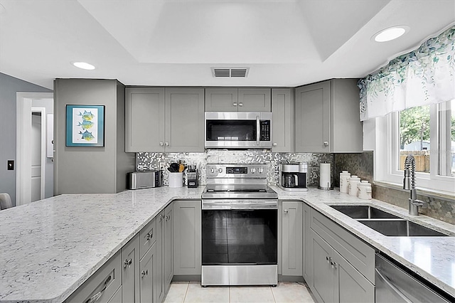kitchen with light stone countertops, gray cabinetry, visible vents, a sink, and appliances with stainless steel finishes