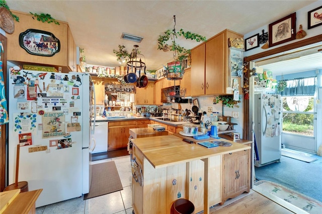 kitchen featuring a peninsula, wood counters, white appliances, and visible vents