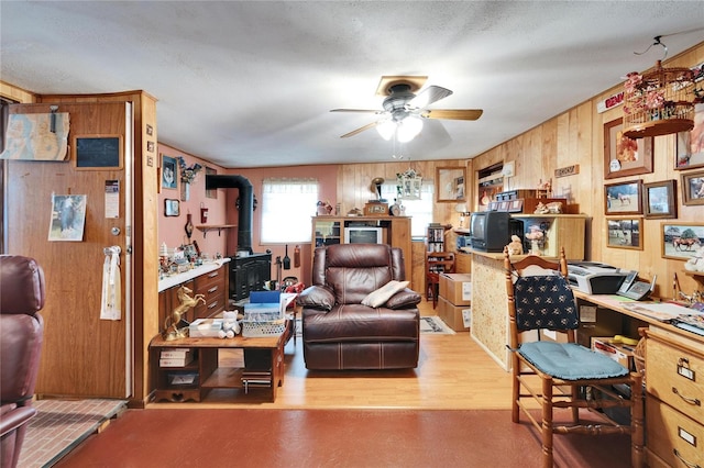 office area with a wood stove, ceiling fan, wood finished floors, and wood walls