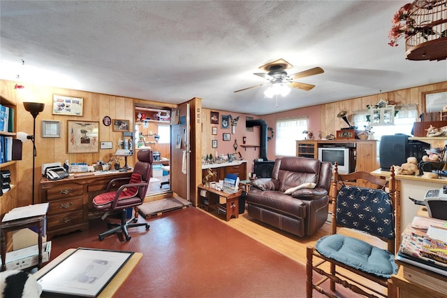 office featuring a wood stove, a textured ceiling, ceiling fan, and wood walls