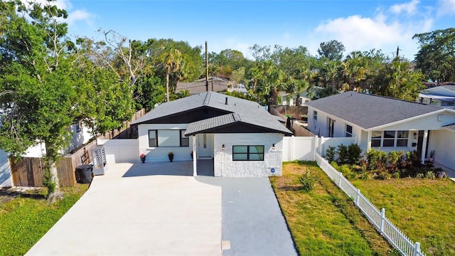 view of front facade featuring concrete driveway, stone siding, and a fenced backyard