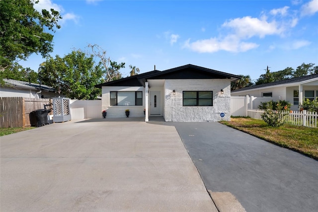 view of front facade featuring stone siding, concrete driveway, and fence