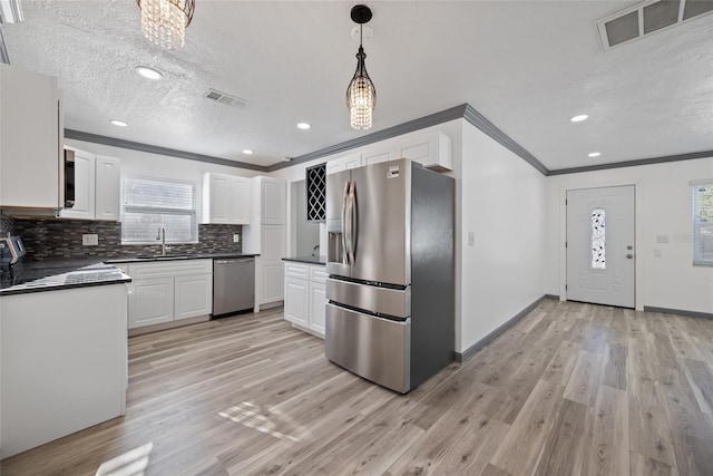 kitchen featuring stainless steel appliances, dark countertops, visible vents, a sink, and crown molding