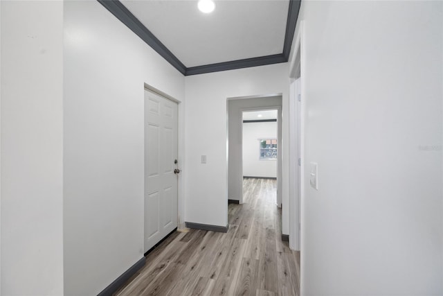corridor featuring light wood-style flooring, crown molding, and baseboards