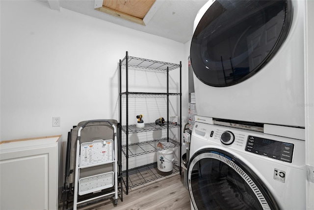 clothes washing area with light wood-style flooring, stacked washing maching and dryer, and laundry area
