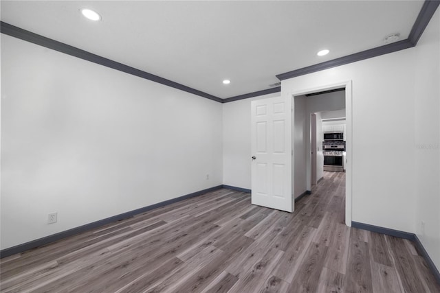 spare room with recessed lighting, wood finished floors, baseboards, and ornamental molding