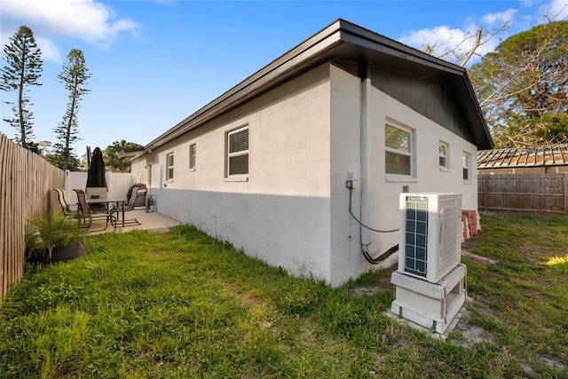 rear view of property with central AC unit, a patio area, a lawn, concrete block siding, and a fenced backyard