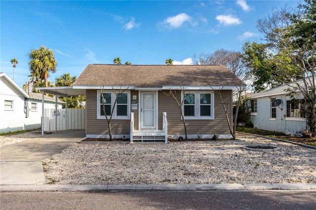bungalow featuring fence, a carport, concrete driveway, and roof with shingles