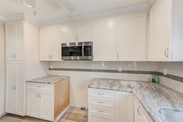 kitchen featuring decorative backsplash, stainless steel microwave, light stone countertops, and ornamental molding
