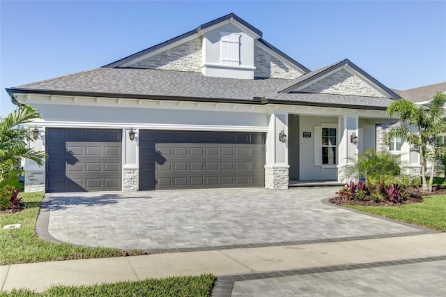 view of front of property featuring an attached garage, decorative driveway, stone siding, and a shingled roof