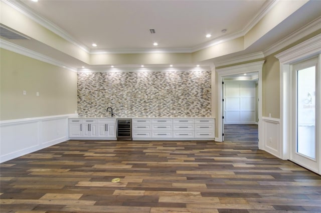 unfurnished room featuring wet bar, crown molding, dark wood finished floors, beverage cooler, and a decorative wall
