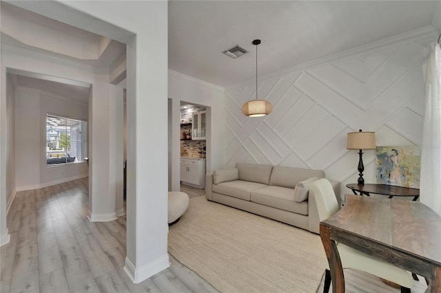 living area with visible vents, baseboards, a decorative wall, crown molding, and light wood finished floors