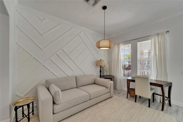 living area featuring baseboards, ornamental molding, a textured ceiling, visible vents, and a decorative wall