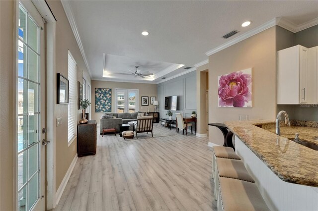 living area featuring crown molding, a tray ceiling, light wood-type flooring, visible vents, and baseboards
