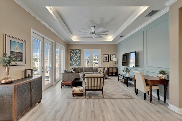 living area featuring visible vents, a raised ceiling, a ceiling fan, crown molding, and light wood finished floors