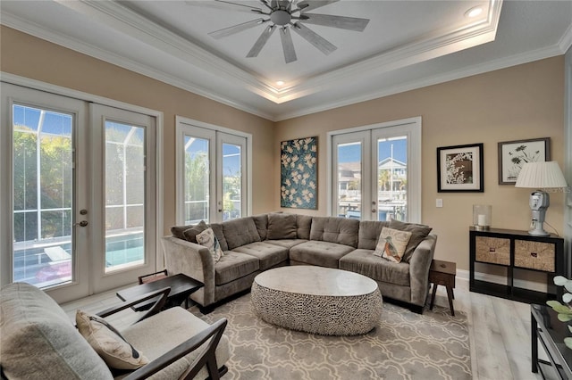 living room with crown molding, light wood-style floors, ceiling fan, a tray ceiling, and french doors