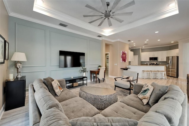 living area with crown molding, visible vents, and a tray ceiling
