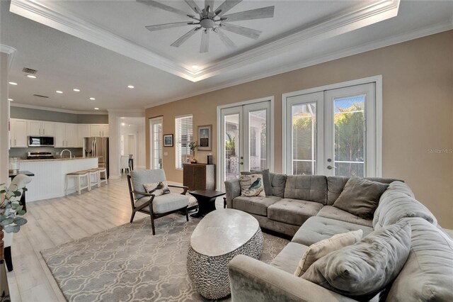 living area with french doors, light wood-style flooring, crown molding, visible vents, and a tray ceiling