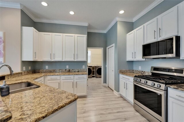kitchen with separate washer and dryer, light wood-type flooring, light stone countertops, appliances with stainless steel finishes, and a sink