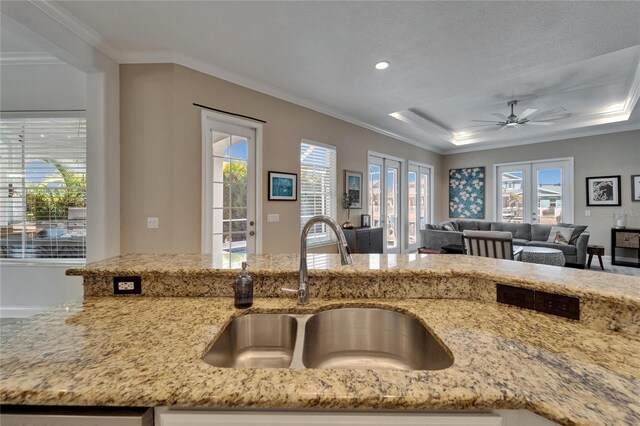 kitchen featuring a sink, open floor plan, a ceiling fan, and light stone countertops