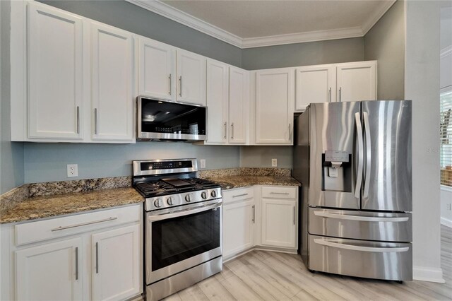 kitchen featuring stone counters, crown molding, white cabinets, light wood-style floors, and appliances with stainless steel finishes