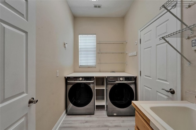 clothes washing area with laundry area, light wood-style flooring, visible vents, a sink, and washer and dryer