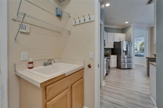 washroom featuring baseboards, light wood-type flooring, crown molding, washer and clothes dryer, and a sink