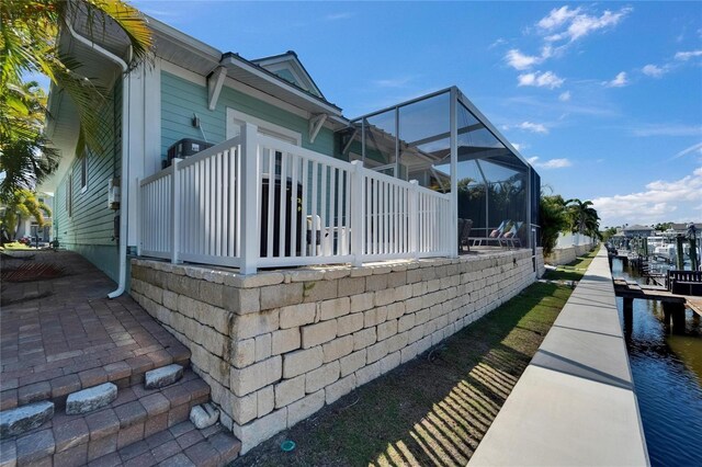 view of side of home with a dock, glass enclosure, and a water view