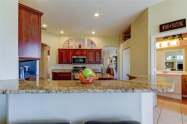 522 Planters Manor Way, Bradenton, FL 34212 - kitchen with stainless steel appliances, reddish brown cabinets, arched walkways, light tile patterned floors, and recessed lighting