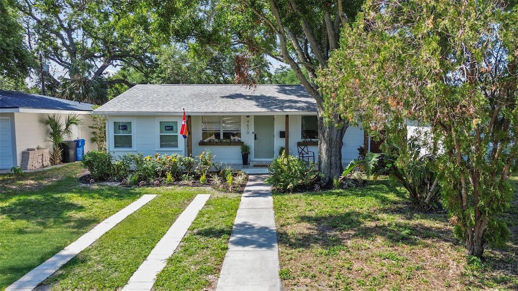 view of front facade with a front yard, a shingled roof, and covered porch