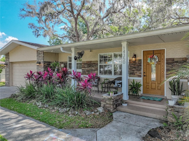 property entrance with driveway, a porch, stone siding, an attached garage, and stucco siding