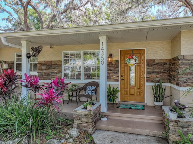 doorway to property with stone siding, covered porch, and stucco siding