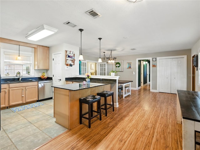 kitchen featuring light brown cabinetry, dark countertops, dishwasher, visible vents, and a sink