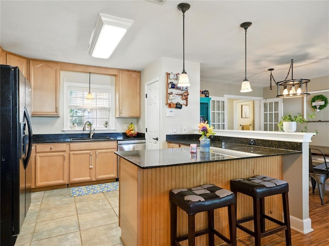 kitchen with light brown cabinets, stainless steel dishwasher, a kitchen breakfast bar, a sink, and black fridge with ice dispenser