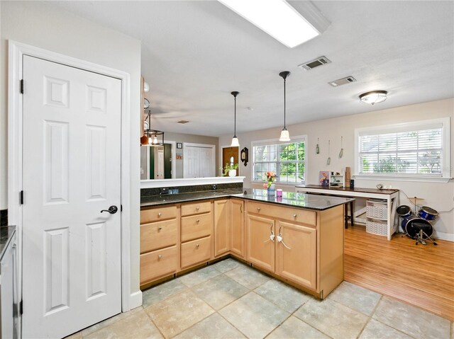 kitchen with dark countertops, visible vents, light brown cabinets, pendant lighting, and a peninsula