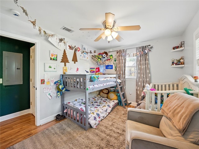 bedroom featuring electric panel, visible vents, baseboards, wood finished floors, and ceiling fan