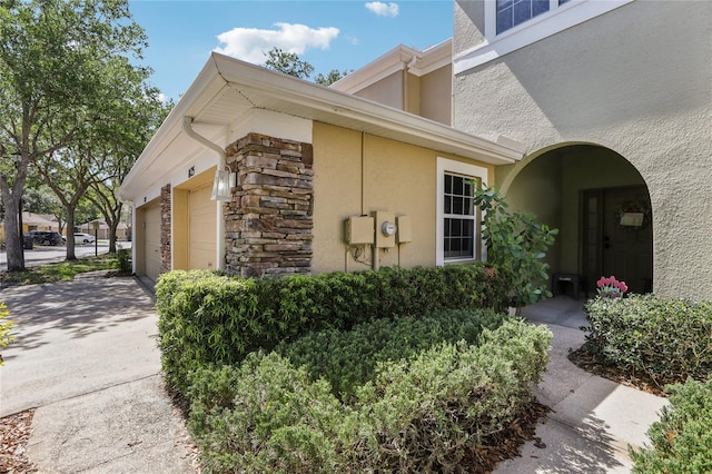 view of property exterior with stucco siding, stone siding, a garage, and concrete driveway