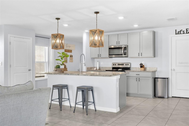 kitchen featuring a sink, visible vents, light stone counters, a breakfast bar, and appliances with stainless steel finishes