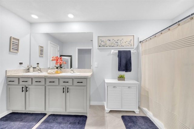 bathroom featuring baseboards, tile patterned flooring, a sink, and double vanity