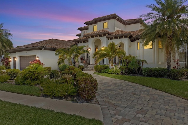 mediterranean / spanish home with an attached garage, a tiled roof, and stucco siding