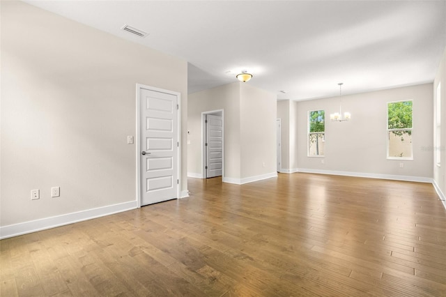 unfurnished room with baseboards, visible vents, wood finished floors, and a chandelier