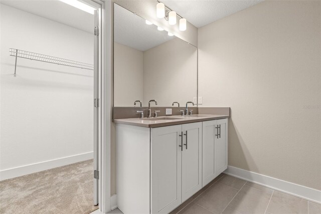 full bathroom with double vanity, a walk in closet, baseboards, and a sink