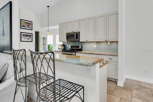 kitchen with stainless steel appliances, a kitchen breakfast bar, backsplash, light stone countertops, and high vaulted ceiling