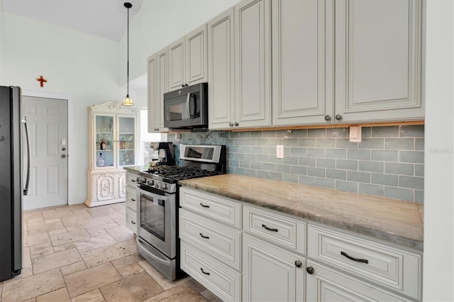 kitchen with stone tile floors, backsplash, light stone countertops, pendant lighting, and appliances with stainless steel finishes