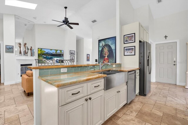 kitchen with high vaulted ceiling, a sink, open floor plan, stone tile flooring, and appliances with stainless steel finishes