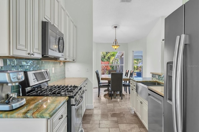 kitchen with tasteful backsplash, stone tile floors, white cabinetry, pendant lighting, and appliances with stainless steel finishes
